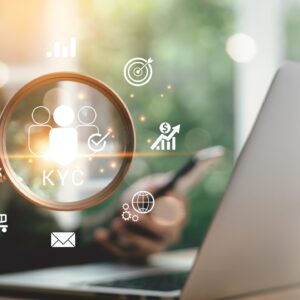 Hand holding a magnifying glass over a laptop with glowing KYC and fintech icons.