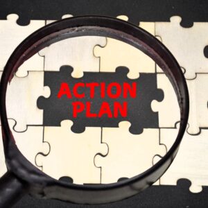 Magnifying glass highlights the red words “ACTION PLAN” over puzzle pieces.