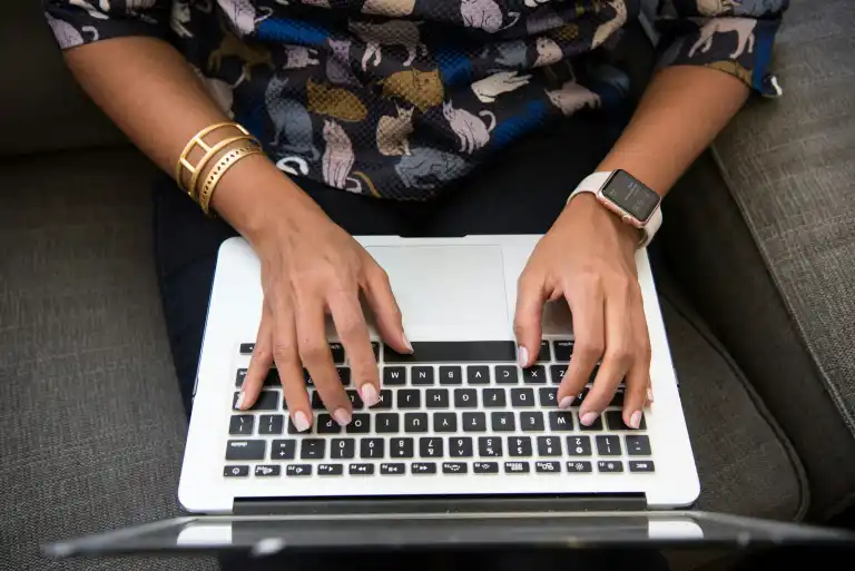 Hands with a watch and bracelet typing on a laptop keyboard.