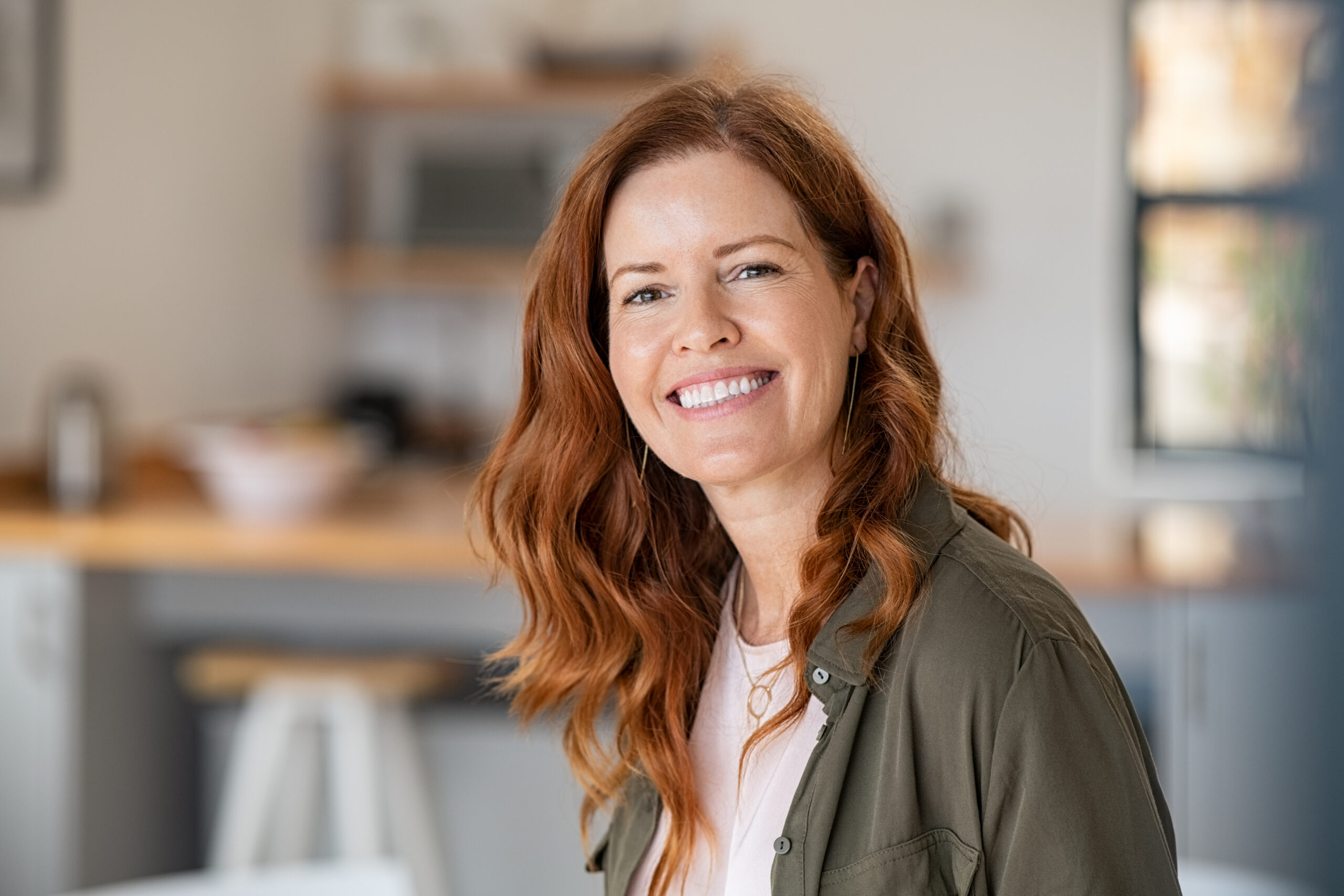 Close-up of a red-haired woman smiling warmly indoors.
