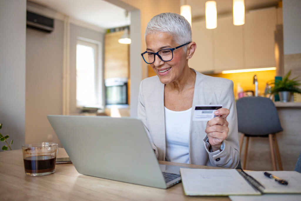 Stylish senior with a silver pixie cut shops online with a credit card and laptop in her kitchen.